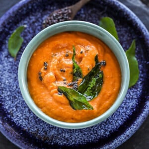 bowl of tomato chutney with curry leaves and mustard seeds thrown in the background