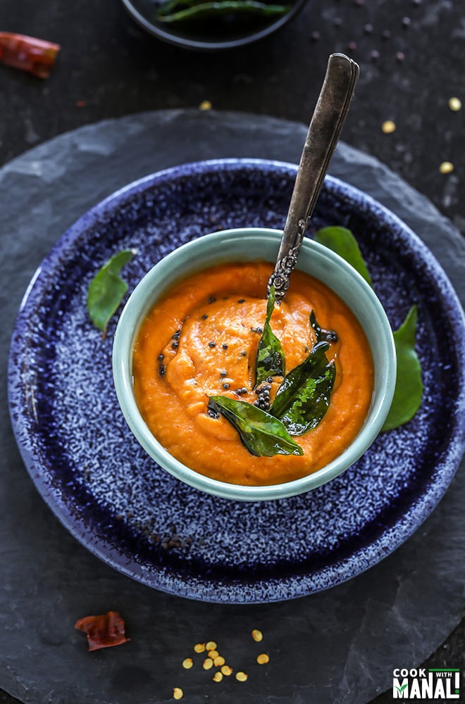 bowl of tomato chutney with a spoon placed on a blue round plate