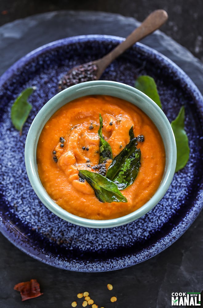 bowl of tomato chutney with curry leaves and mustard seeds thrown in the background