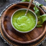 green color chutney served in a copper bowl with mint leaves, cilantro scattered in the background