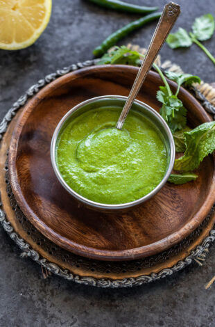 green color chutney served in a copper bowl with mint leaves, cilantro scattered in the background