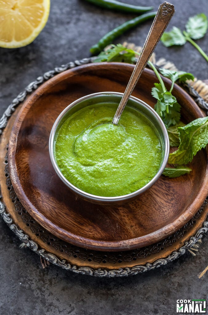 green color chutney served in a copper bowl with mint leaves, cilantro scattered in the background