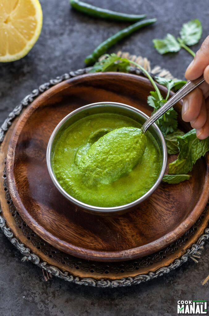 a spoon digging into a bowl of green color chutney