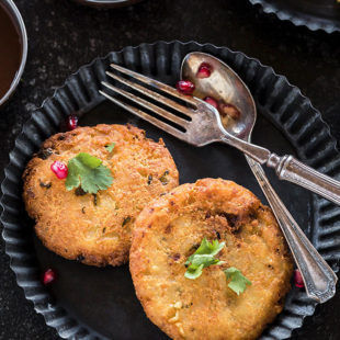 two pieces of aloo tikki in a rimmed plate along with a spoon and fork