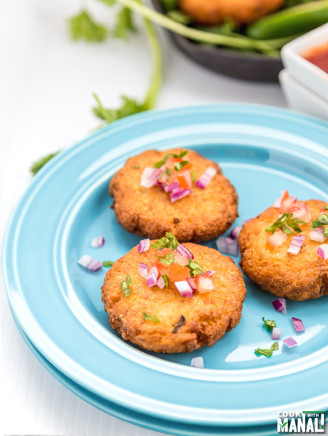 three pieces of aloo tikki served in a blue plate and garnished with cilantro and onion