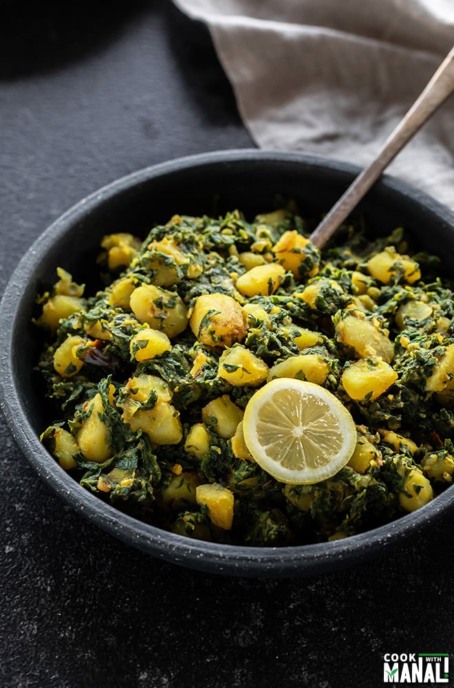 aloo palak in a black bowl with a spoon and served with a lemon wedge