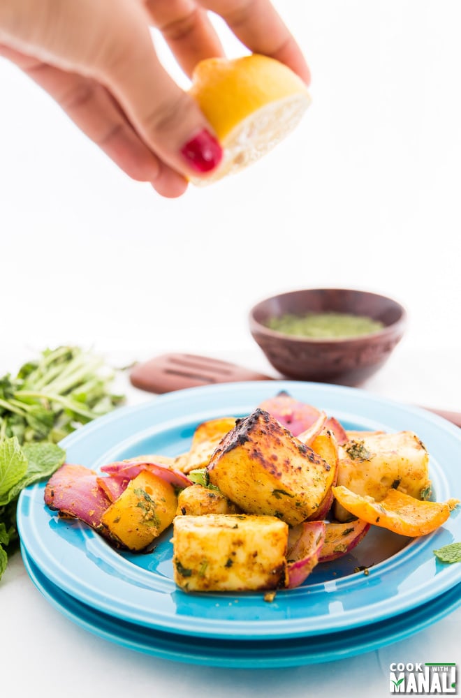 grilled paneer tikka in a blue plate with lemon being squeezed into it