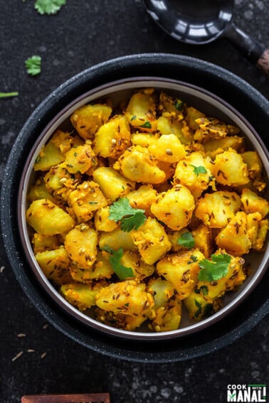 jeera aloo in a black bowl with a black wooden ladle on the side