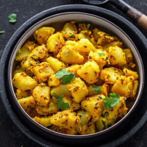 jeera aloo in a black bowl with a black wooden ladle on the side