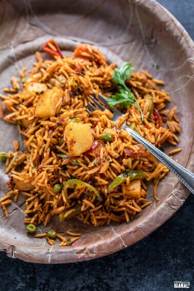 rice with vegetables like potato, pepper garnished with cilantro served in a paper plate