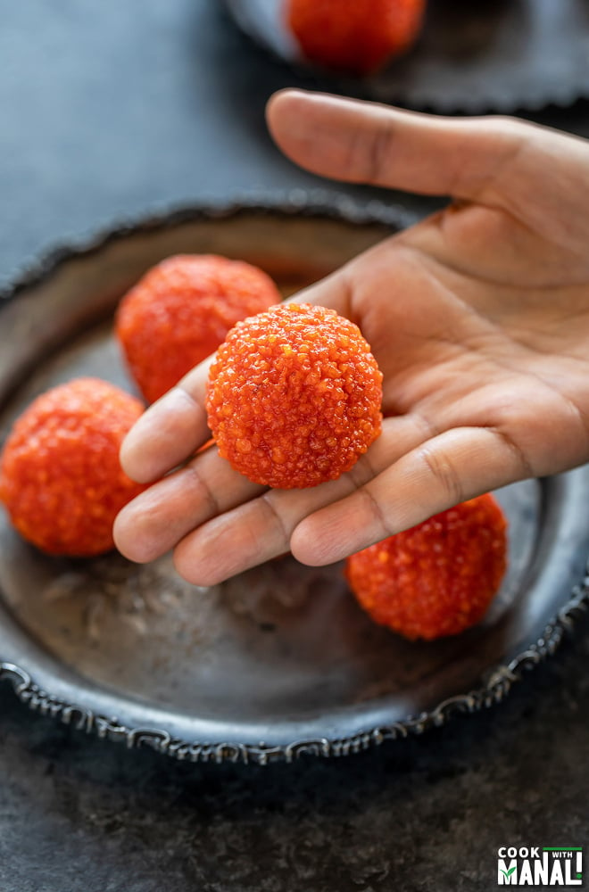 motichoor ladoo placed on an extended palm with more ladoos placed in a plate in the background