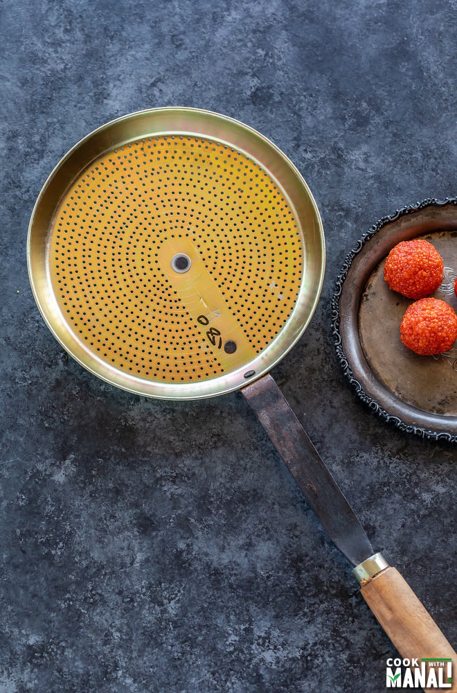 ladoo jhara (ladle) made of brass and iron placed on a board with few ladoos seen on the side