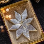 kaju katli arranged in a sweet box with small lights on the side and plate of cashews in the background