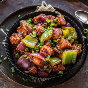 restaurant style chilli paneer served in black plate and brown rice served in the background