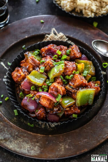 restaurant style chilli paneer served in black plate and brown rice served in the background