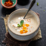 raita served in a white bowl topped with mango and garnished with mint