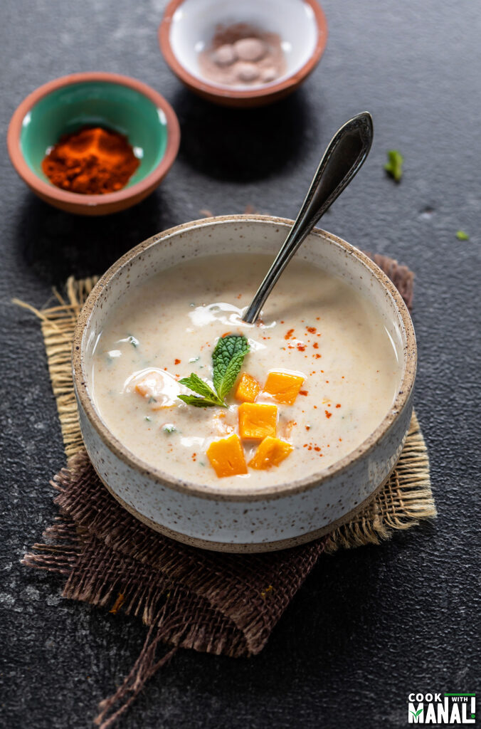 raita served in a white bowl topped with mango and garnished with mint