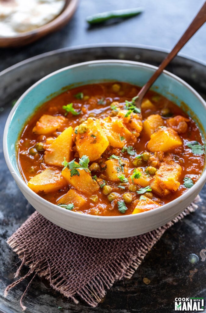 spoon digging into a bowl of potatoes and peas curry