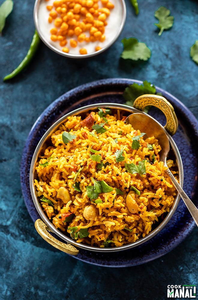 tomato rice in a copper kadai with a spoon with bowl of yogurt in the background