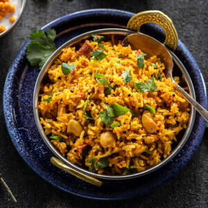 tomato rice in a copper kadai with a spoon with bowl of yogurt in the background