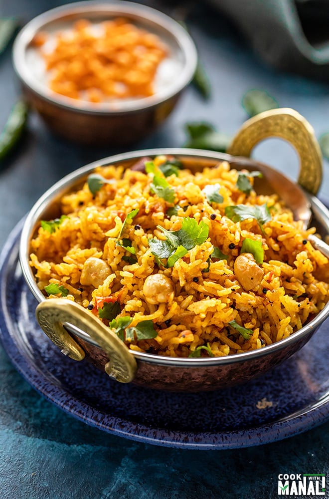 tomato rice in a copper kadai with a spoon with bowl of yogurt in the background