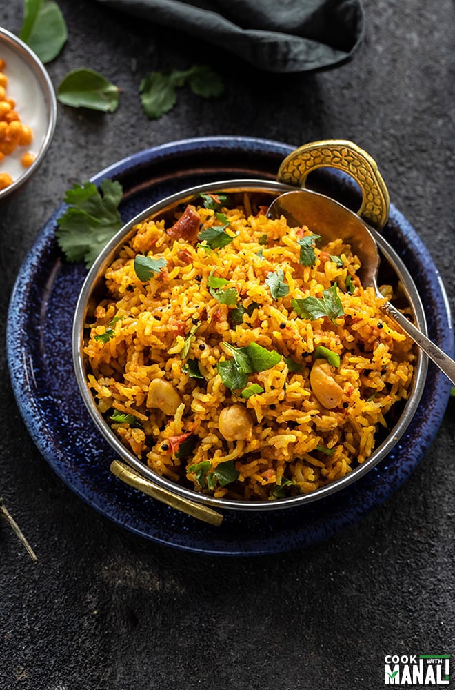 tomato rice in a copper kadai with a spoon with bowl of yogurt in the background