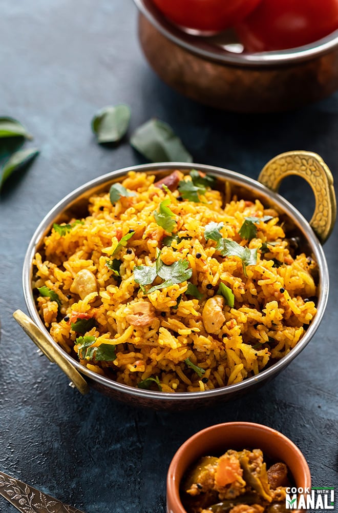 tomato rice in a copper kadai with curry leaves in the background