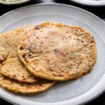 3 aloo parathas on a white plate with a bowl of yogurt in the back