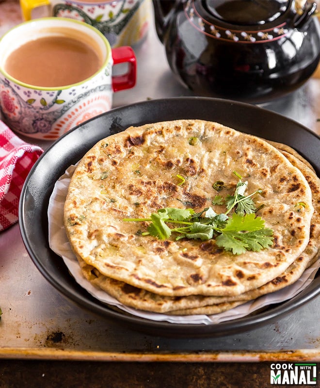 stack of parathas on a plate with cup of chai in the background