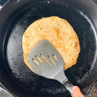 spatula pressing a paratha to cook it