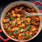 kadai paneer in a red color wok with a wooden spatula with blue napkin in the background