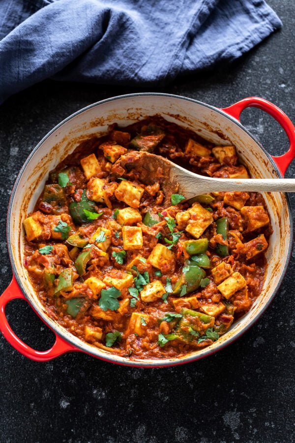 kadai paneer in a red color wok with a wooden spatula with blue napkin in the background