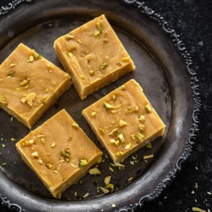 4 pieces of besan burfi arranged on a round silver antique plate