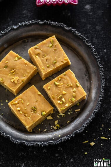 4 pieces of besan burfi arranged on a round silver antique plate