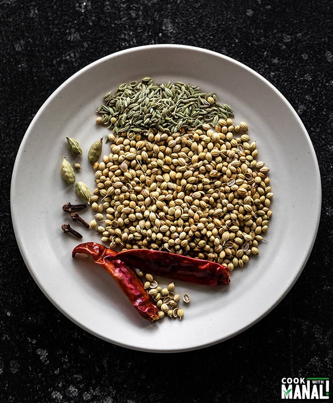 spices like coriander seeds, red chilies, cardamom and fennel seeds in a white plate