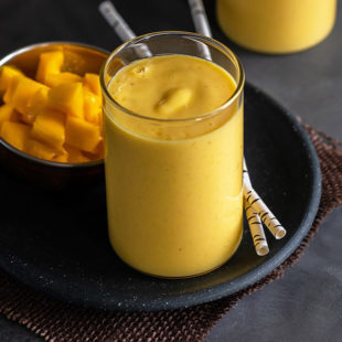 mango lassi served in a glass with 2 straws and another glass of mango lassi in the background