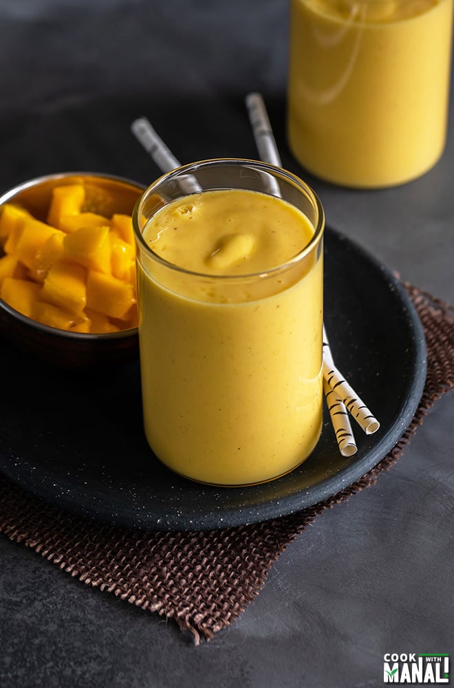 mango lassi served in a glass with 2 straws and another glass of mango lassi in the background