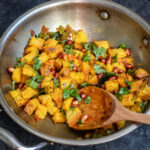 cubes of bread tossed with masala in a kadai with a wooden spatula on side