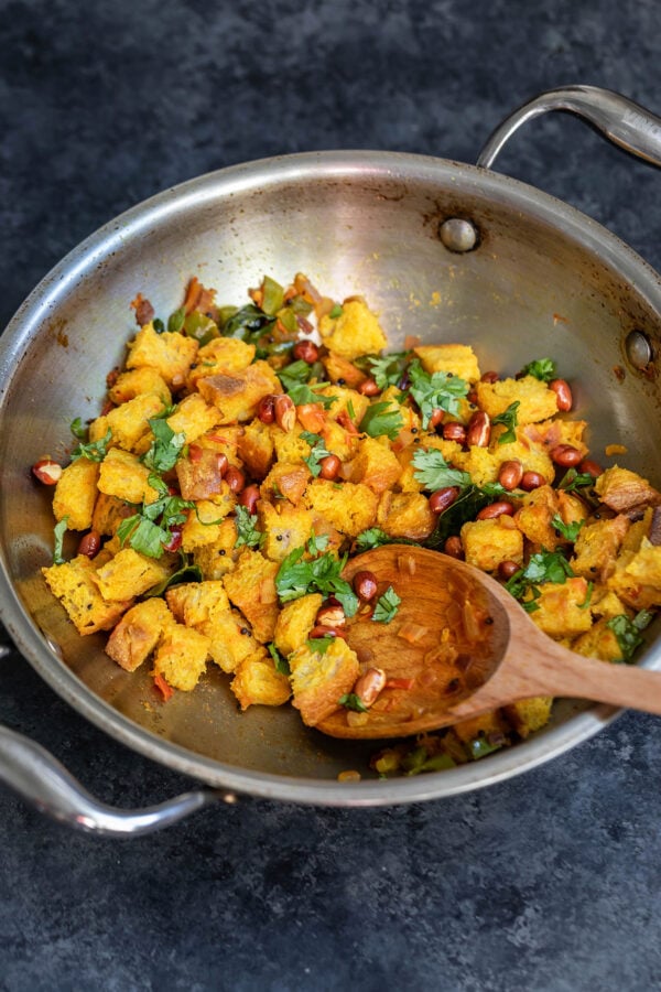 cubes of bread tossed with masala in a kadai with a wooden spatula on side