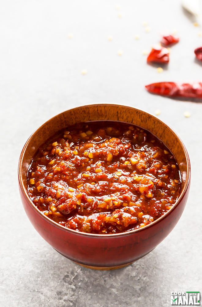 schezwan sauce in a red bowl with some broken chilies in the background