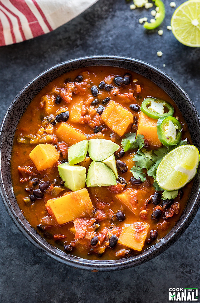 a bowl of butternut squash chili topped with avocado, cilantro and lime