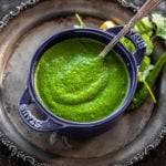 cilantro chutney served in a blue bowl with a spoon and some cilantro leaves on the side