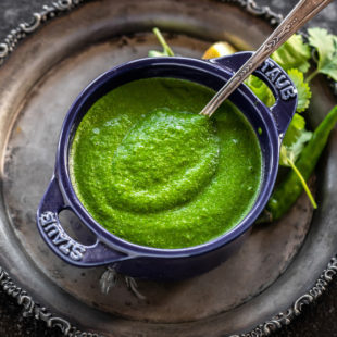 cilantro chutney served in a blue bowl with a spoon and some cilantro leaves on the side