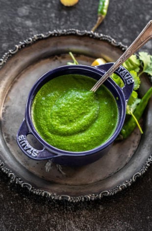 cilantro chutney served in a blue bowl with a spoon and some cilantro leaves on the side