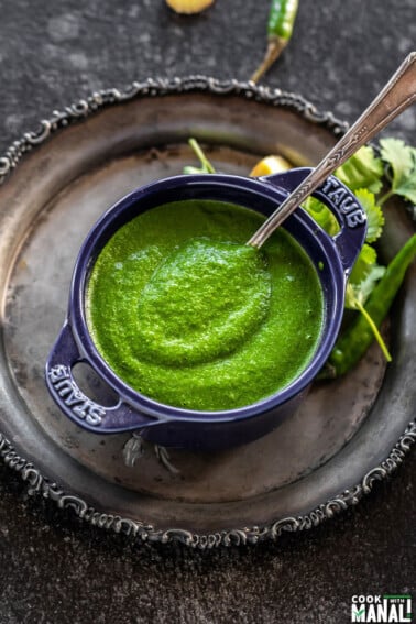 cilantro chutney served in a blue bowl with a spoon and some cilantro leaves on the side