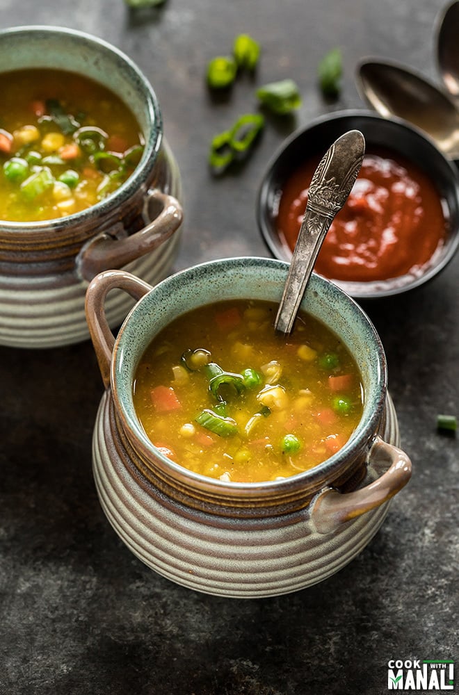 a bowl of sweet corn soup with a spoon and a small bowl of hot sauce in the background