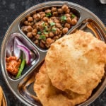 two bhaturas and chole in a steel plate with sliced onions and pickle