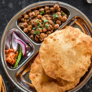 two bhaturas and chole in a steel plate with sliced onions and pickle