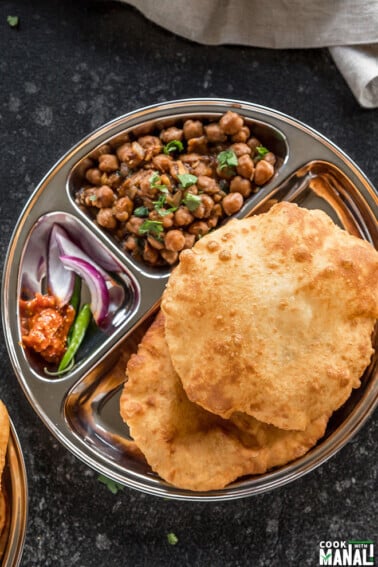 two bhaturas and chole in a steel plate with sliced onions and pickle