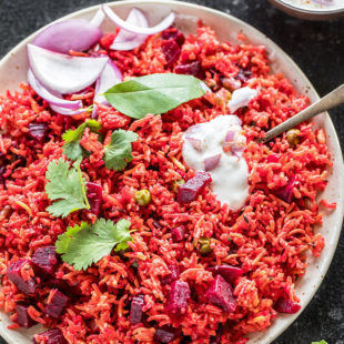 beetroot pulao in a white plate garnished with cilantro and a dollop of yogurt on top